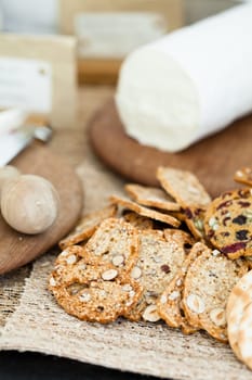 Closeup of dry crackers with cheese on wooden cutting board in background