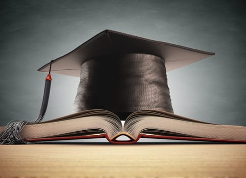 Graduation cap over the book with blackboard on background. Clipping path included.