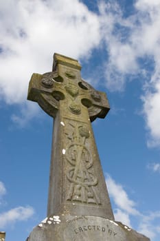 an old celtic cross in an irish graveyard with blue cloudy sky