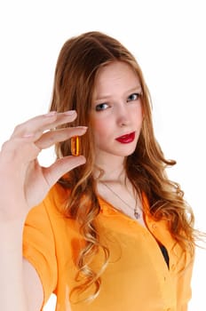 A serious looking young woman in a yellow blouse showing a big vitamin.capsule, looking sceptical, isolated for white background..