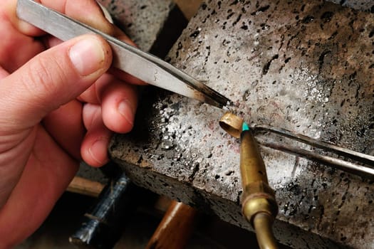 Skilled hands that create handmade jewelry with gold processing.