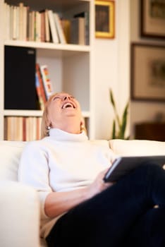 portrait of beautiful old woman using tablet pc and smiling, sitting on sofa at home