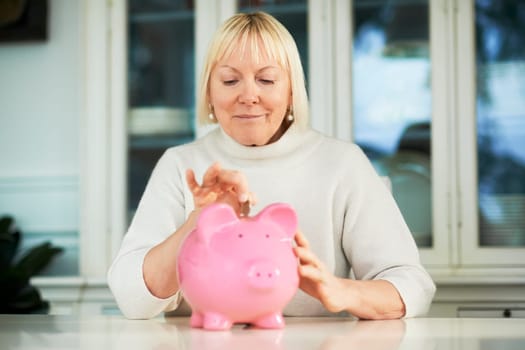 portrait of happy caucasian senior woman saving euro coin into piggybank and smiling