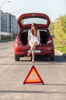 Sexy helpless woman sitting near broken red car