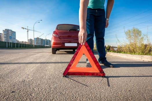 Young man placing red triangle sing on road after car crash