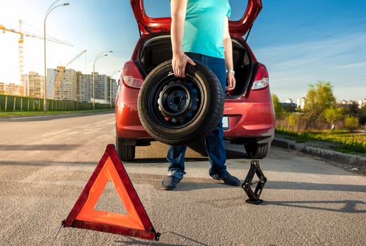 Photo of man holding spare wheel against broken car