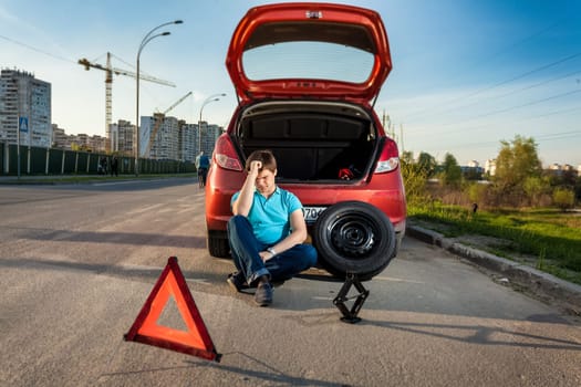 Portrait of depressed man leaning against broken car