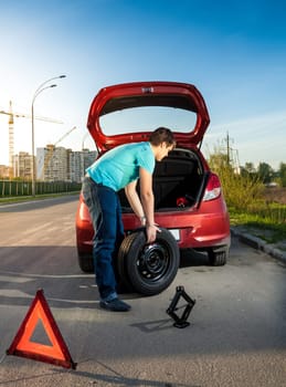 Photo of man changing punctured wheel on broken car