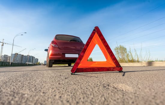Closeup photo of red triangle sign on road next to broken car