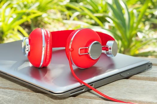 Vivid red headphones and laptop on the wooden bench in park