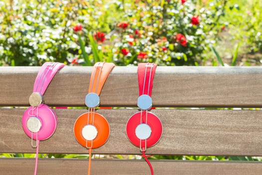 Three varicolored headphones of different colors no wood bench in park