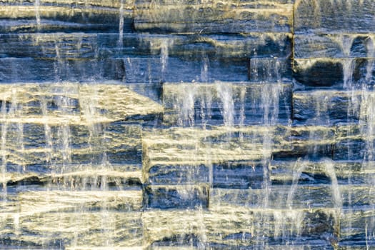 Flowing water over dark stone wall with spot backlight