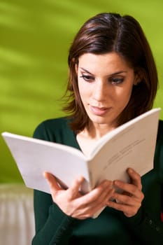 young caucasian woman reading book at home, sitting on sofa