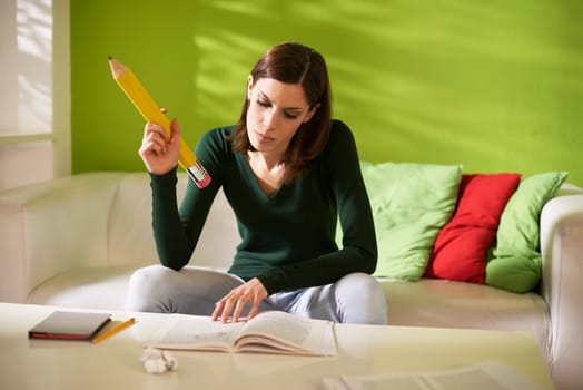 young caucasian student doing homeworks and taking notes on book with huge pencil at home