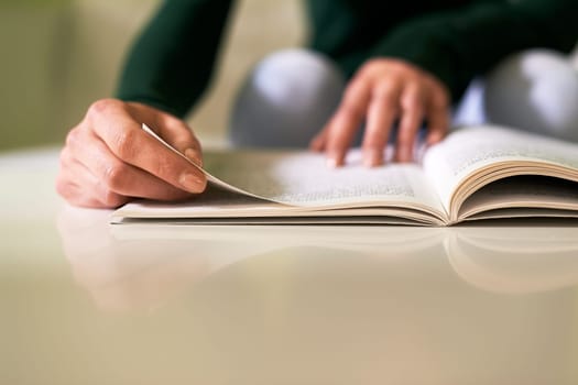 young caucasian woman reading book at home, sitting on sofa. Copy space on table