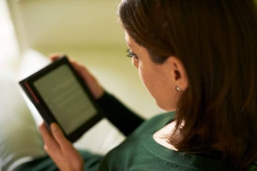 young caucasian woman reading ebook at home, sitting on sofa and smiling