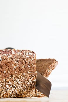 Still life with wholemeal bread and bread knife on cutting board against a bright background