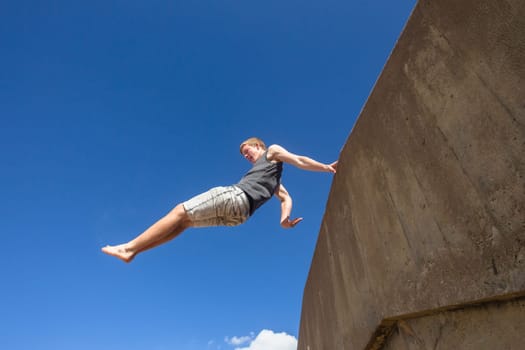 Teen boy jumping off wall into summersault flights off concrete wall parkour on beach