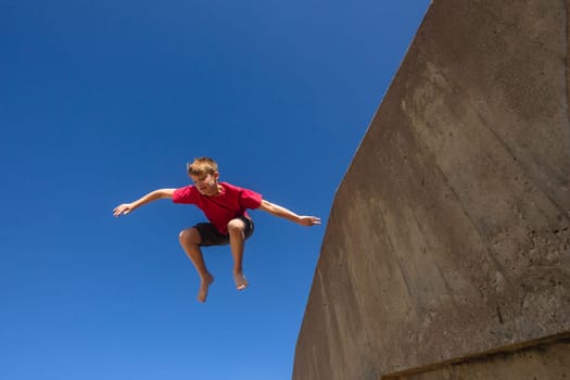 Teen boy jumping off wall in parkour off wall on beach