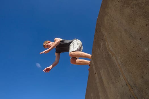 Teen boy jumping off wall into summersault flights off concrete wall parkour on beach