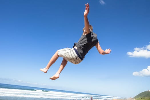Teen boy jumping off wall into summersault flights off concrete wall parkour on beach