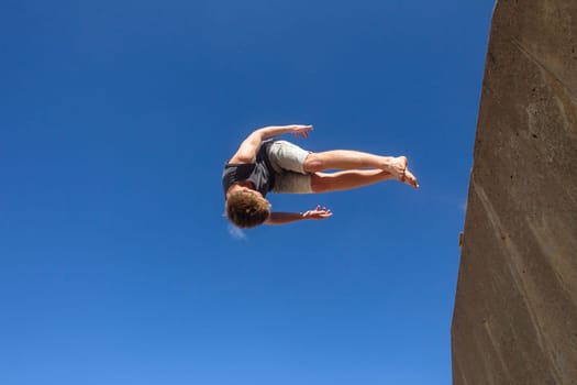 Teen boy jumping off wall into summersault flights off concrete wall parkour on beach