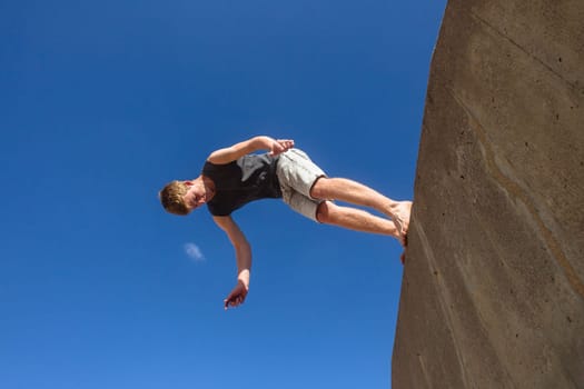 Teen boy jumping off wall into summersault flights off concrete wall parkour on beach