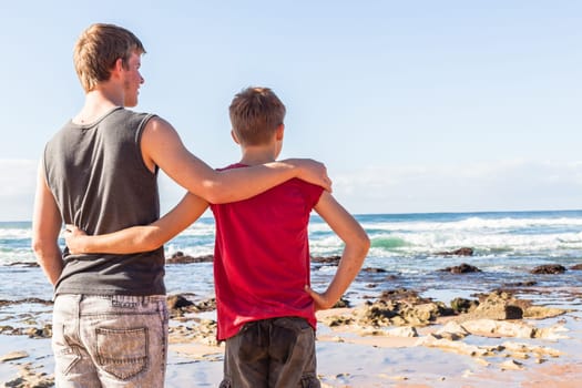 Teen boys family hangout playtime at the  beach ocean on clear blue day