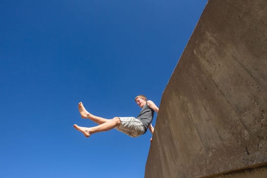 Teen boy jumping off wall into summersault flights off concrete wall parkour on beach