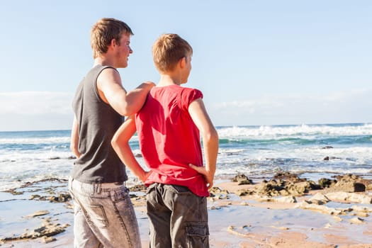 Teen boys family hangout together at the  beach ocean on clear blue day