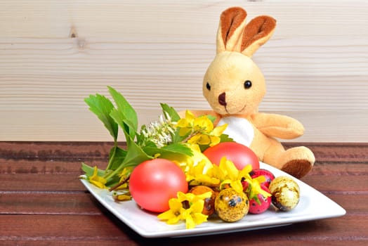 Easter eggs, spring flowers and a rabbit toy on a wood table