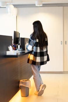 One young caucasian brunette woman with flowing hair in a plaid shirt is standing behind the reception desk in a dentistry, close-up side view.