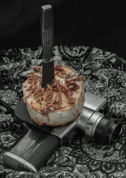 The black metal knife is inserted into the Caramel Pecan topped with caramel frosting and pecans on the old movie camera 8mm with dark background. Copy sapce, Selective focus.