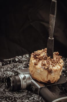 The black metal knife is inserted into the Caramel Pecan topped with caramel frosting and pecans on the old movie camera 8mm with dark background. Copy sapce, Selective focus.