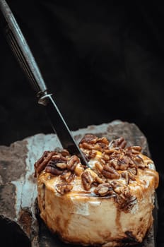 The black metal knife is inserted into the Caramel Pecan topped with caramel frosting and pecans on rock with dark background. Copy space, Selective focus.