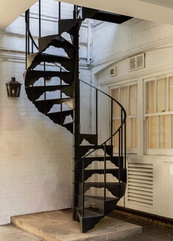 London, UK - Oct 24, 2023 - Vertical view of Black metal spiral staircase pattern with iron railing lead from the ground floor to the upper floor on the side of white brick wall. Ladder decoration exterior, Space for text, Selective focus.