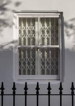 House exterior with wooden casement window on white wall with wrought iron fence. White steel folding gates in glass window, The sunshine lights through the glass window frame, Space for text, Selective focus.