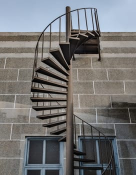 Brown metal spiral staircase with iron railing lead down from Rooftop balcony to the first floor in front of brick textured wall. Selective focus.
