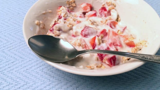 Closeup of yogurt with cereal and strawberries on a light blue background.