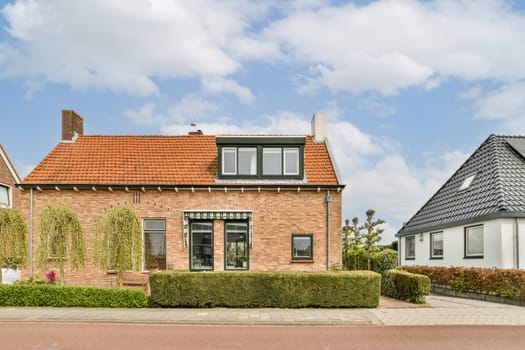 a house in the netherlands with red tiled roof and white brick walls, surrounded by green hedges against blue sky