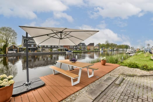 an outdoor area with tables and umbrellas on the side of the water in front of a row of houses