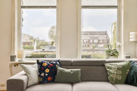 a living room with two large windows, and a couch in front of the window looking out onto the street