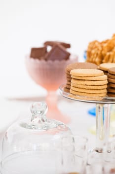 Closeup of stacks of dry biscuits on glass serving stand with chocolate pieces and waffle cookies in bowls in background