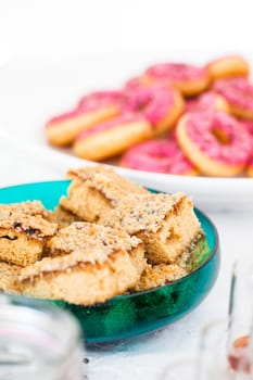 Closeup of slices of dry cake in glass serving bowl with pink colored donuts in bowl in background