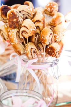 Closeup of small snack sized cinnamon buns on sticks in a glass jar with decorative ribbon tied in bow