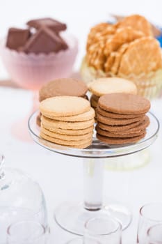 Closeup of four stacks of dry biscuits on glass serving stand with chocolate pieces and waffle cookies in bowls in background
