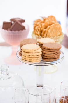 Closeup of four stacks of dry biscuits on glass serving stand with chocolate pieces and waffle cookies in bowls in background