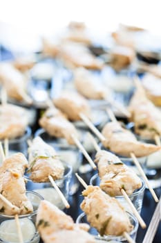 Closeup of pieces of cooked chicken on wooden skewers with mayonnaise based condiment in small glasses