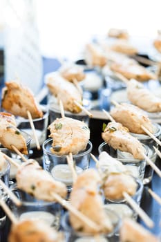 Closeup of pieces of cooked chicken on skewers with mayonnaise based condiment in glasses