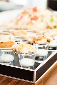 Closeup of pieces of cooked chicken on wooden skewers with mayonnaise based condiment in small glasses in serving tray